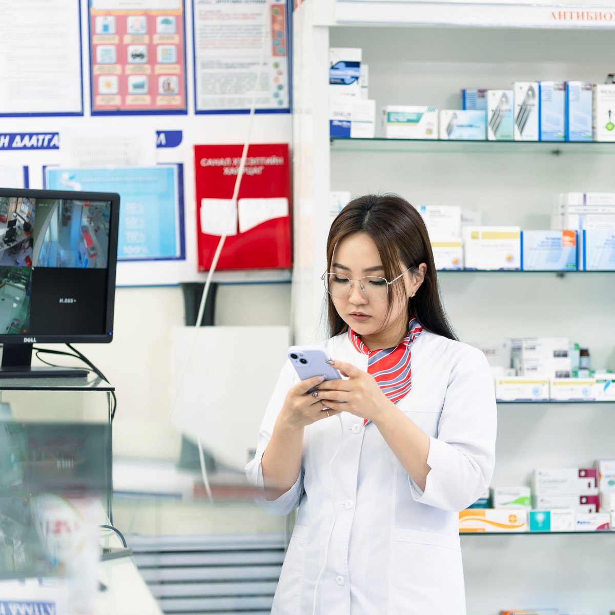 Une pharmacienne consulte son téléphone au comptoir de son officine