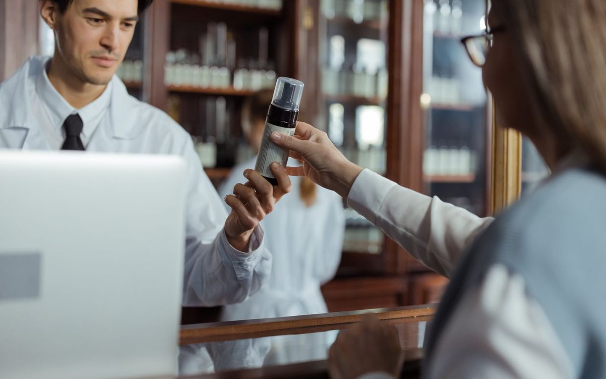 Au comptoir d’une officine, un pharmacien tend un produit à une consœur