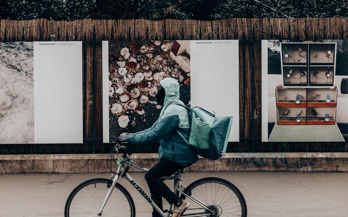 Un coursier à vélo, sac de livraison sur le dos, le long d’un mur
