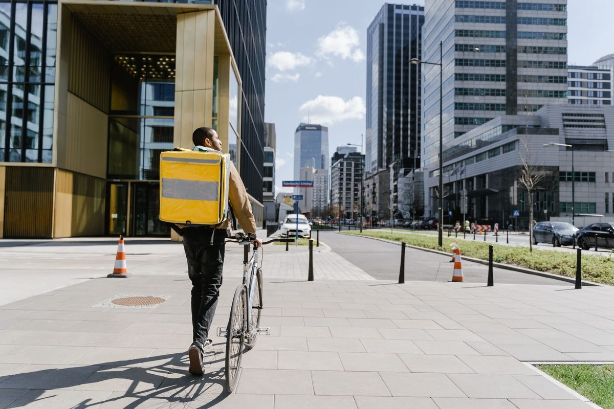 Un coursier à vélo, sac de livraison sur le dos, dans une rue de ville