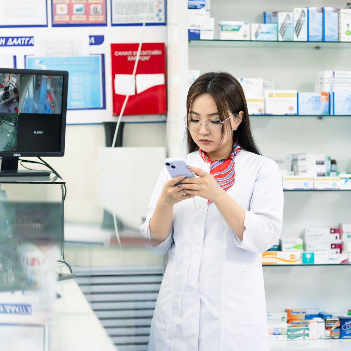 Une pharmacienne répond à un message client sur son téléphone, au comptoir